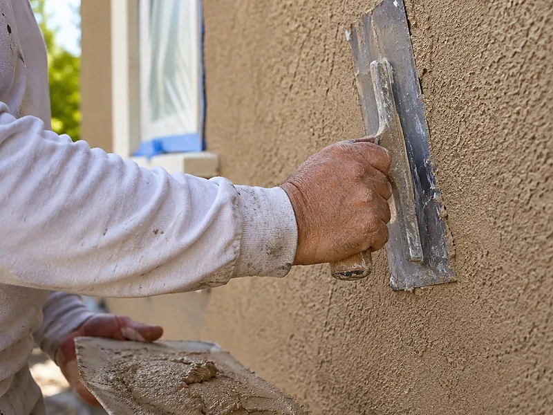 Hawk and trowel loaded with tan finish coat at a wall