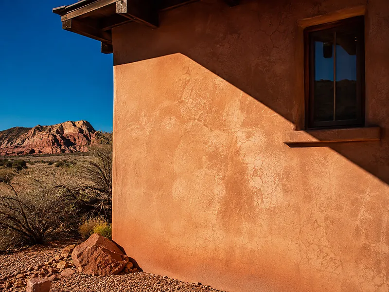 Sun-beaten stucco wall against red rock, its color faded by exposure